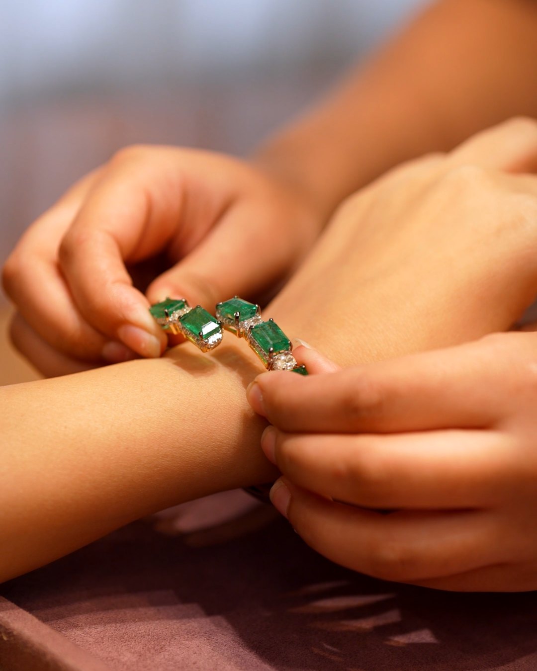 Emerald and diamond bangle being fastened on the wrist